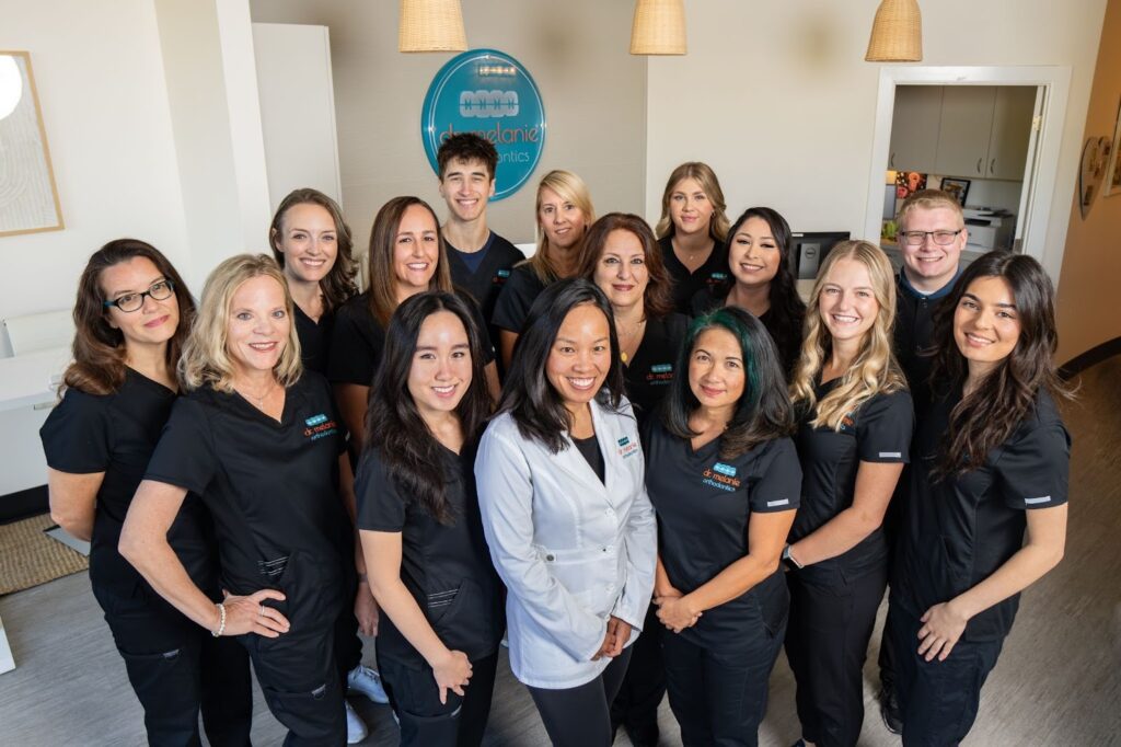 Team of orthodontic professionals at Dr. Melanie Orthodontics, smiling and wearing black scrubs, in a welcoming office setting, promoting personalized orthodontic care for retainers and smile maintenance in Rancho Santa Fe and San Diego.